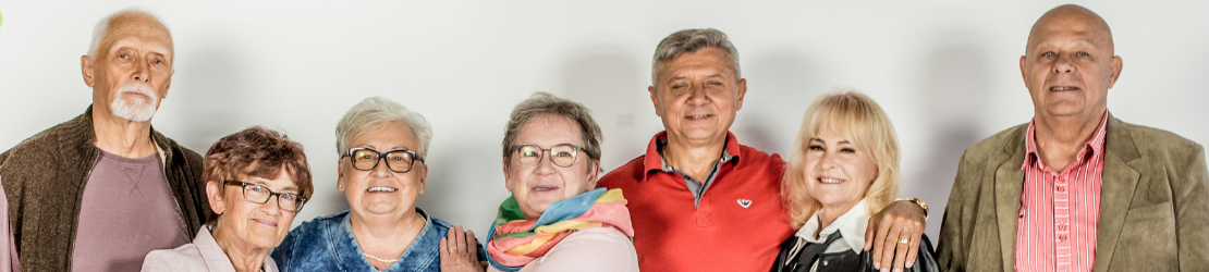 Grupa uśmiechniętych seniorów i seniorek pozuje do zdjęcia. Obejmują się i śmieją. 